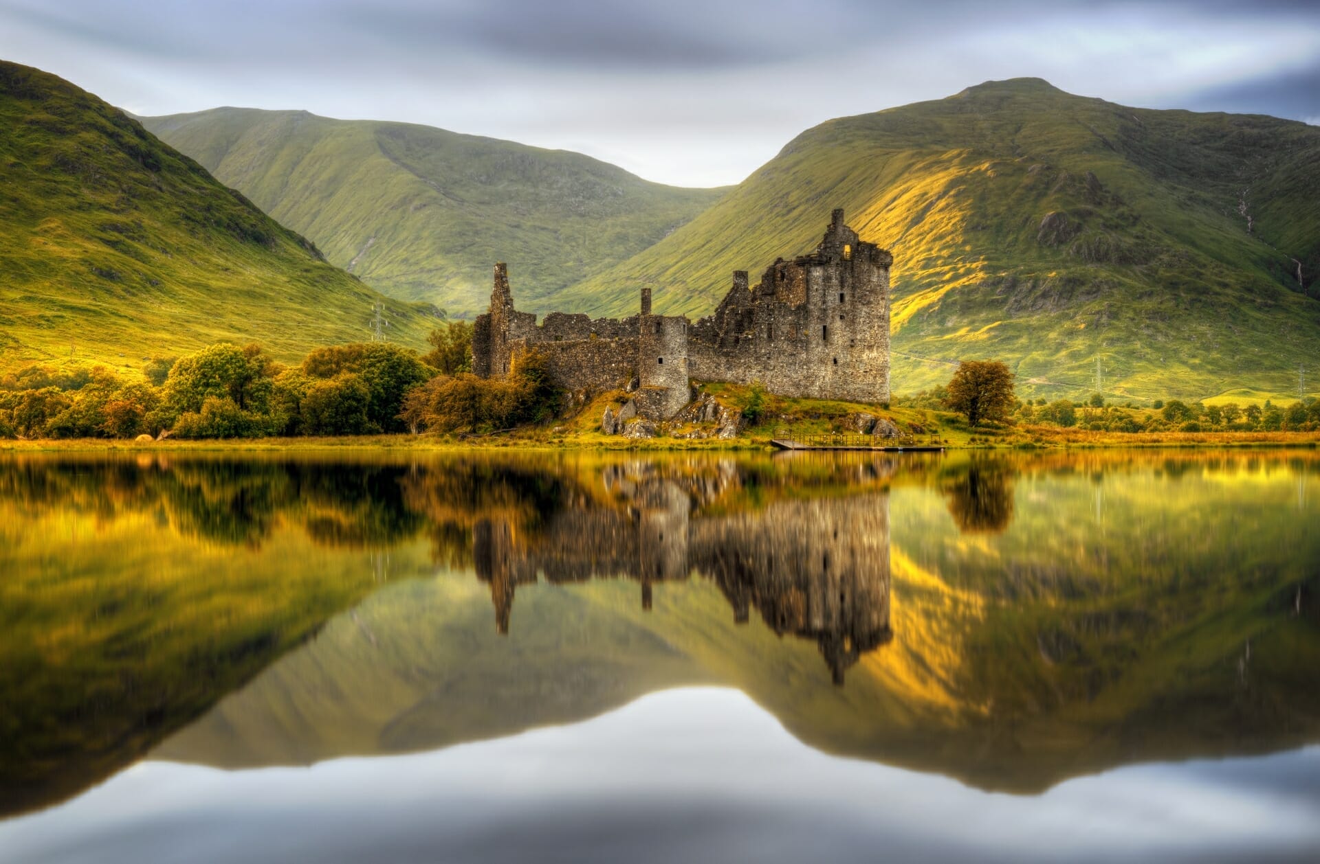 Ein Schloss und die sanfte Hgellandschaft spiegeln sich in perfekter Symmetrie im See